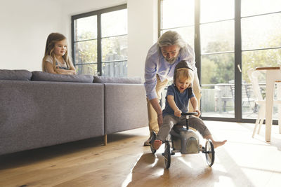 Grandfather playing with grandchildren, sitting on toy car