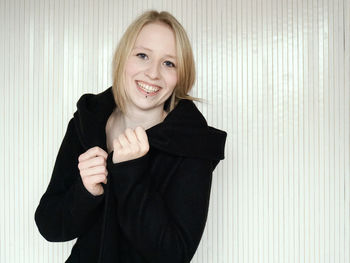 Portrait of smiling young woman standing against curtain