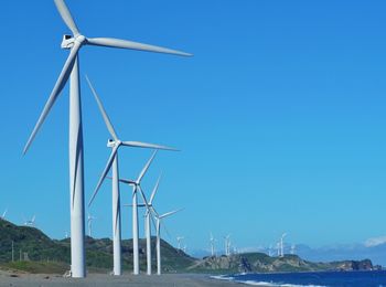 Wind turbines on landscape against clear blue sky