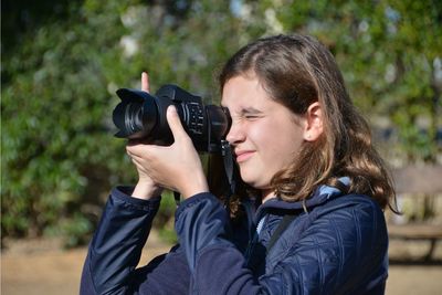 Close-up of girl photographing against trees