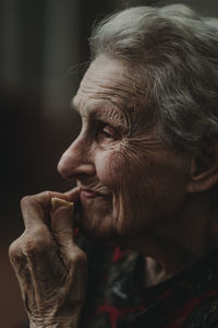 Side view of thoughtful elderly woman with gray hair touching wrinkled face and thinking about past while eating a cookie