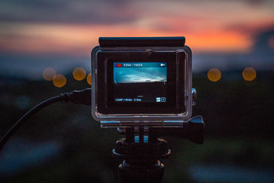 Close-up of illuminated camera against sky during sunset