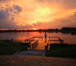 Man standing on pier over lake against sky during sunset