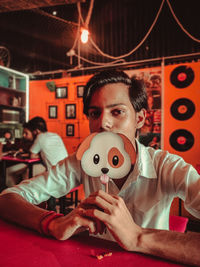 Portrait of young man holding prop while sitting in restaurant