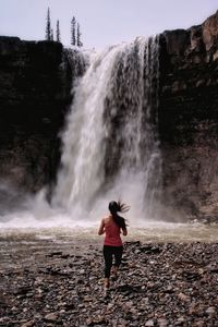 Rear view of woman running towards waterfall
