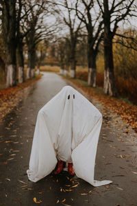 Little ghost standing on the road in red boots. autumn halloween