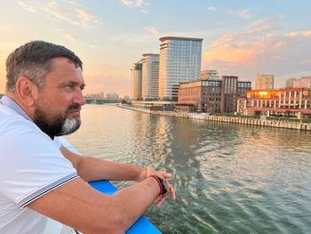 Side view of man looking at river against sky during sunset