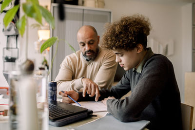 Father guiding son doing homework while sitting at table