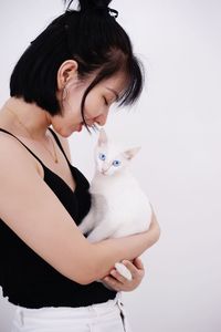 Smiling young woman holding cat while standing against white background