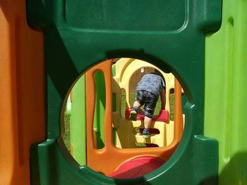 Rear view of boy playing on jungle gym seen through hole