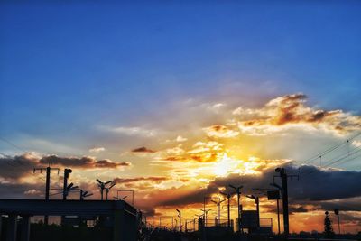 Silhouette factory against sky at sunset