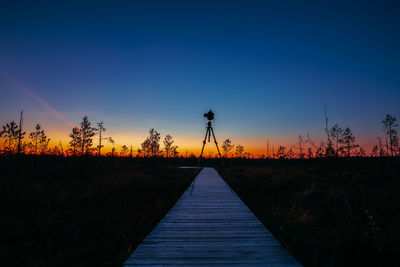 Boardwalk on field against clear sky at sunset