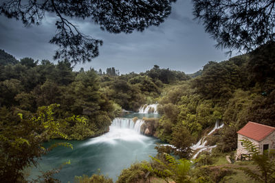 Scenic view of waterfall amidst trees against sky