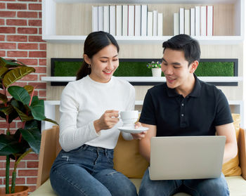 Young woman using phone while sitting on laptop