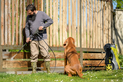 Man spraying water on wooden fence in yard