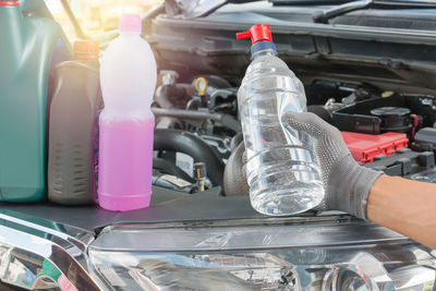 Close-up of mechanic hand holding bottle by car engine