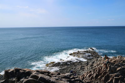 High angle view of man photographing coupe on rocks against sea