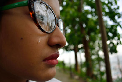 Close-up side view of young woman crying against trees