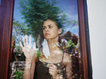 Portrait of young woman looking through window