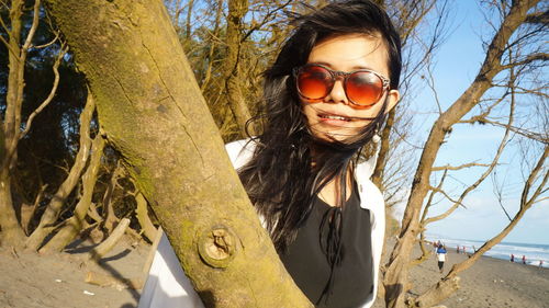 Young woman wearing sunglasses by tree trunk at beach