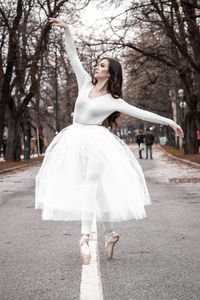 Young woman dancing on white umbrella against trees