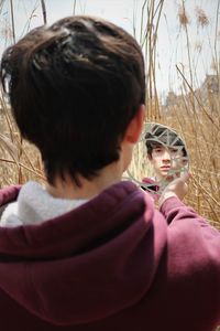 Rear view of young man looking at his reflection in mirror