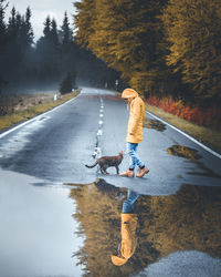 Side view full length of young woman standing by puddle and cat on road