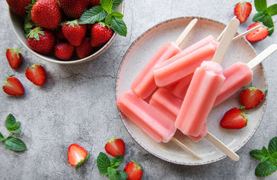 Homemade frozen strawberry ice cream popsicles and fresh strawberries on a concrete background. 