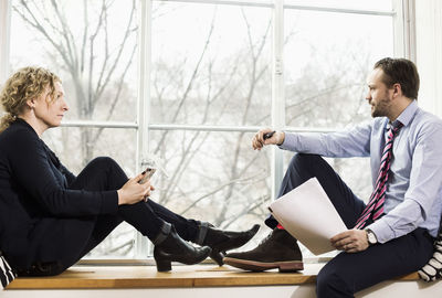 Full length of business people sitting on ledge by window