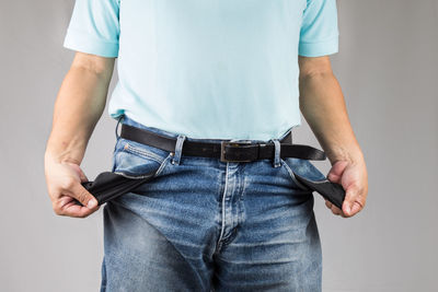 Midsection of man showing empty pockets against gray background