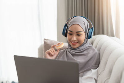 Portrait of young woman using phone while sitting on bed at home