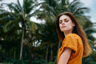 Portrait of beautiful young woman standing against trees