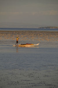 Full length of man paddle boarding in sea against sky