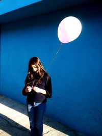 Full length portrait of woman standing against blue wall