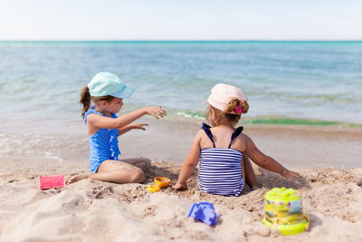 Girls playing with sand while sitting at beach