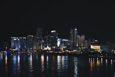 Illuminated city reflecting in river against clear sky at night