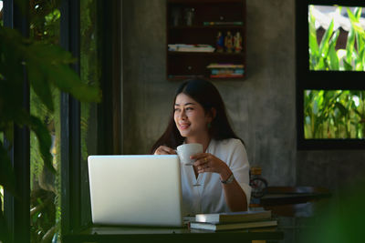 Young woman using phone while sitting on table