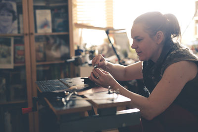 Girl master processes the metal copper plate on the workbench in the home workshop, soft focus 