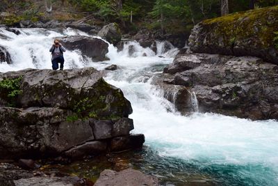 Man photographing while crouching on rock by waterfall at forest