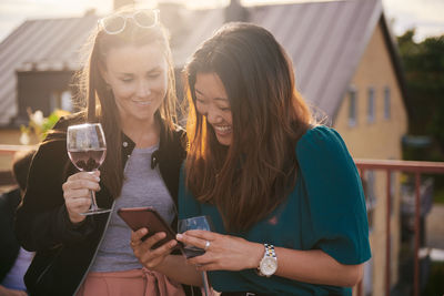 Cheerful woman showing her mobile phone to female friend on terrace during sunset