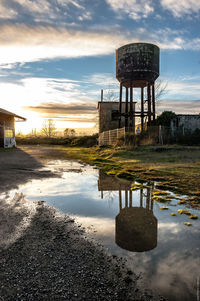 Reflection of storage tank on water against cloudy sky