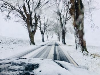 Snow covered road amidst trees during winter