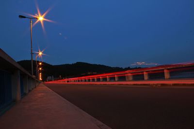 Illuminated road against clear sky at night