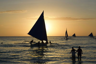 Silhouette people on sea against sky during sunset