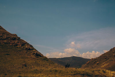 Man riding horse on mountain against sky