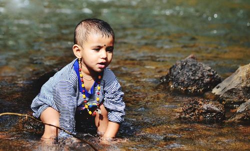 Boy sitting on rock in river