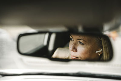 Businesswoman with in-ear headphones seen in rear-view mirror reflection of car