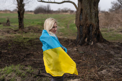 Side view of woman standing with ukrainian flag on field