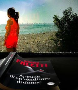 Rear view of woman in car by sea against sky
