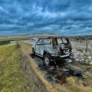 View of abandoned car on field against sky